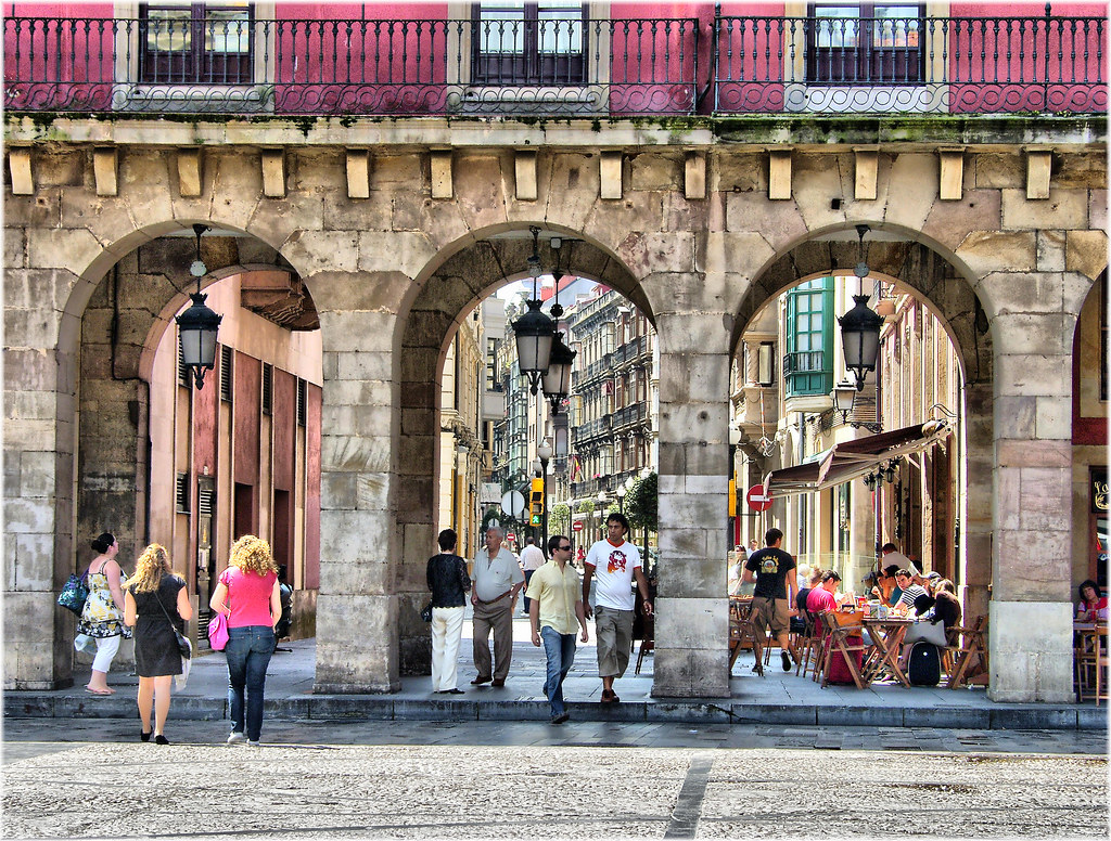 Gente paseando bajo los soportales de la Plaza Mayor de Gijón